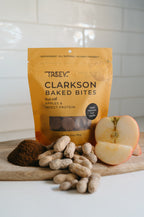 TREEV Clarkson Baked Bites bag with a halved apple, peanuts and powdered protein on a wooden board