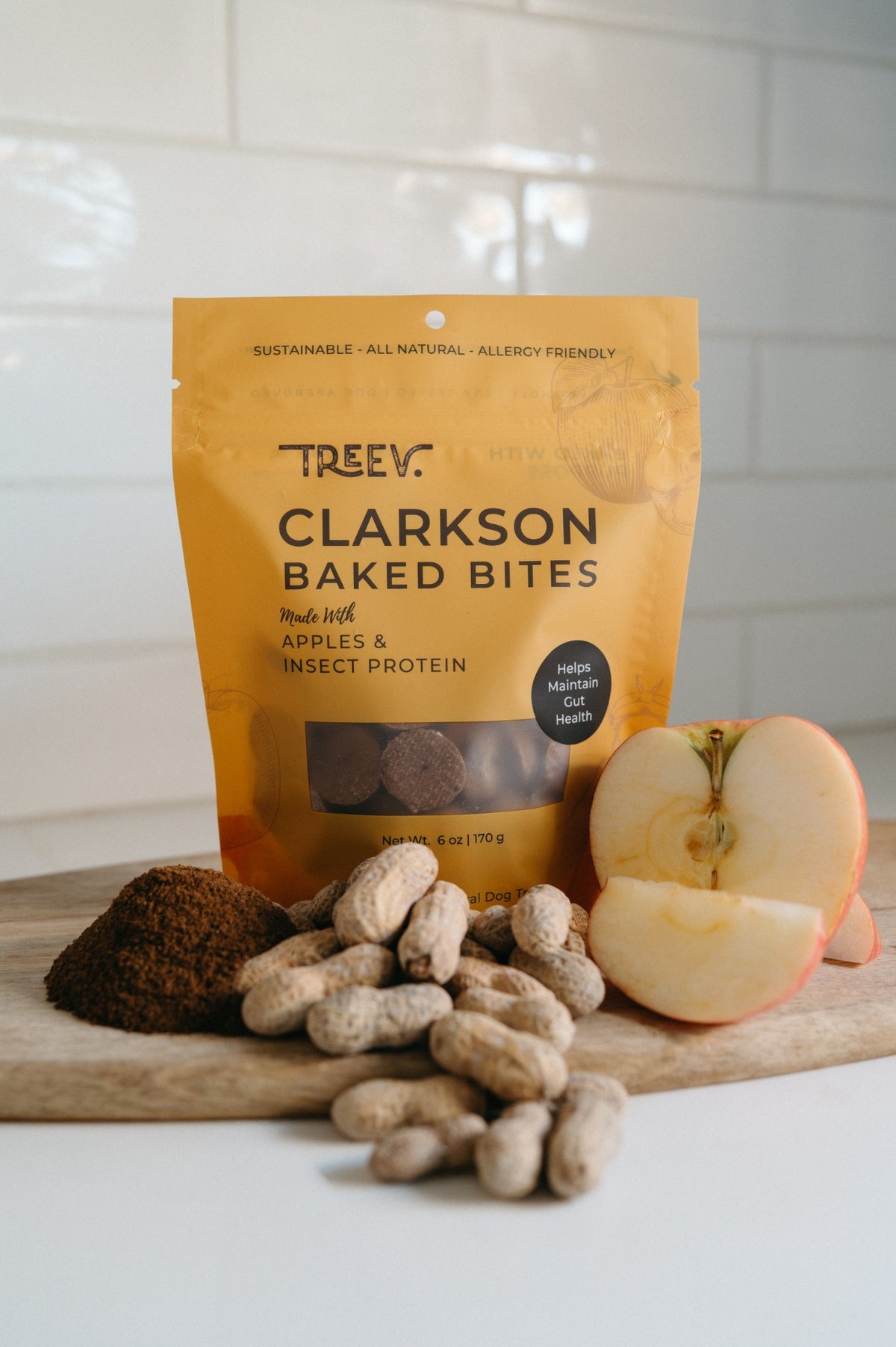 TREEV Clarkson Baked Bites bag with a halved apple, peanuts and powdered protein on a wooden board